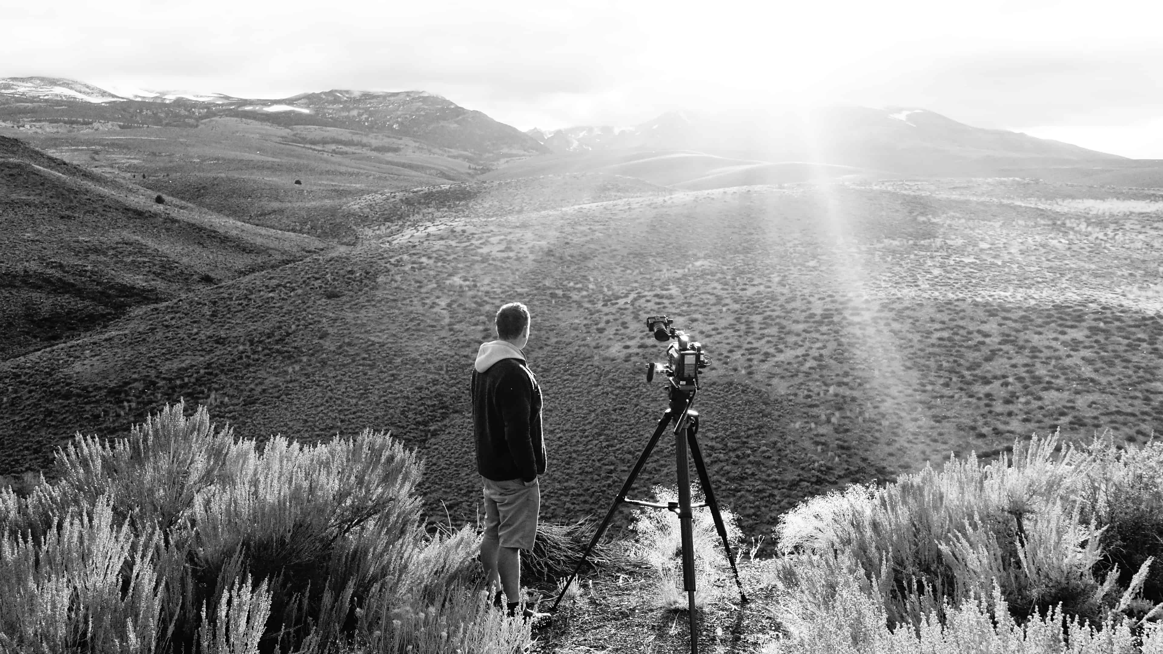 Felix Greif mit Stativ-Kamera bei Dreharbeiten in einer Berglandschaft im Gegenlicht