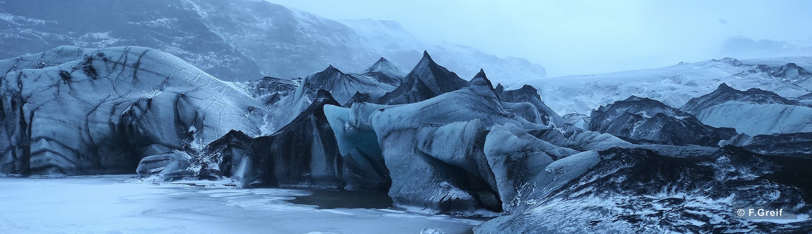 Blaues Gletschereis vor verschneiten Bergen